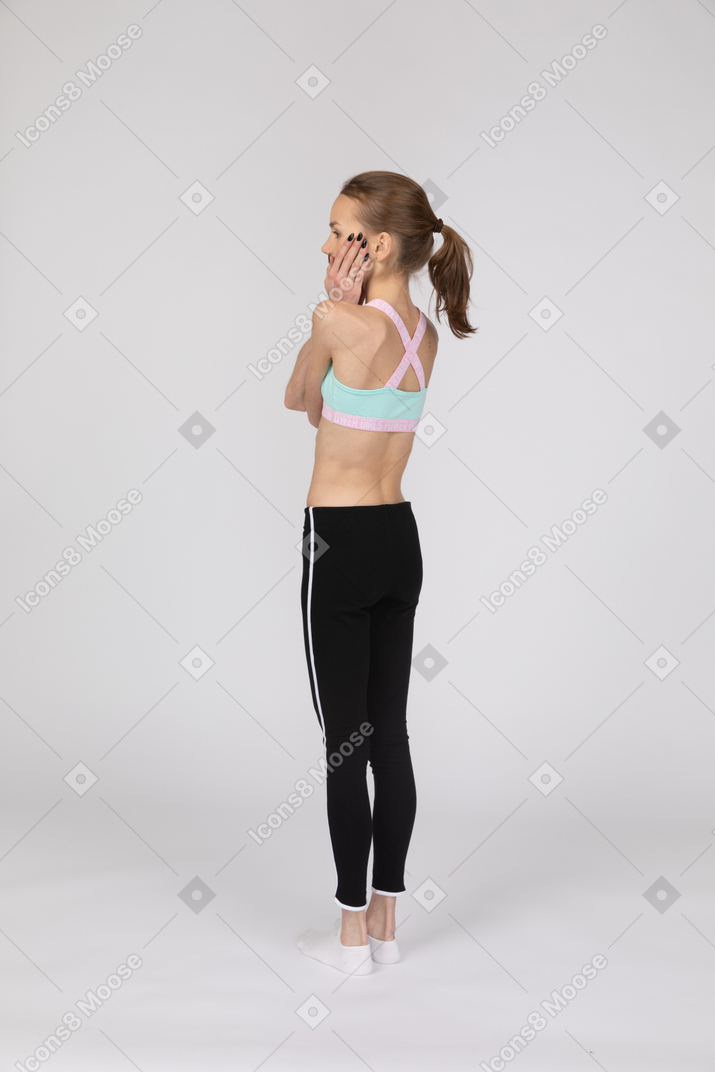 Three-quarter back view of a teen girl in sportswear hiding her mouth