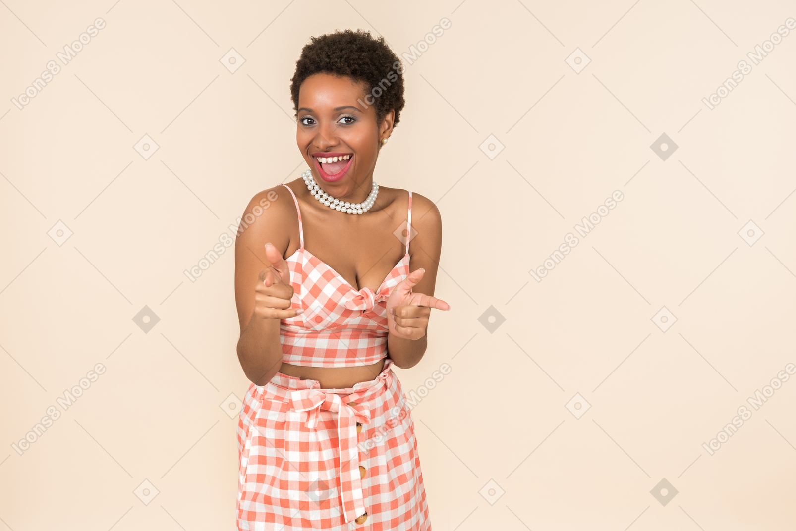 Jovem mulher de cabelo curto preto em um top xadrez e uma saia, posando contra um fundo peachy simples