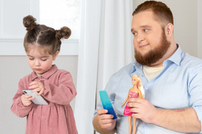 A man holding a barbie doll looking at a little girl using smartphone