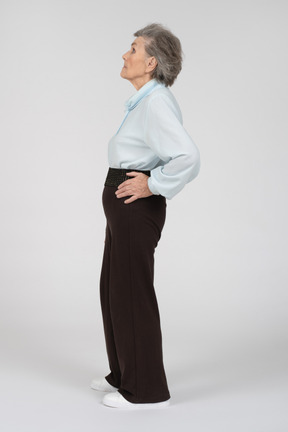 Vue latérale d'une vieille femme regardant dans l'expectative avec la main sur sa hanche
