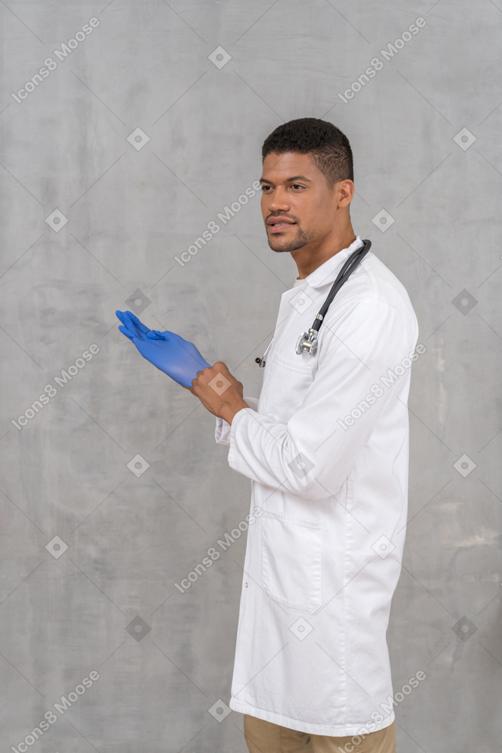 Vista lateral del médico varón poniéndose guantes médicos