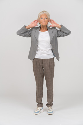 一位身着西装的老妇人双手放在头后站立的前视图