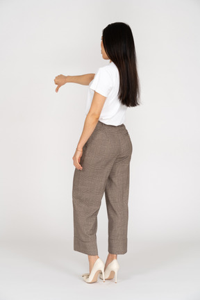 Vista posteriore di tre quarti di una giovane donna in calzoni e maglietta che mostra il pollice verso il basso