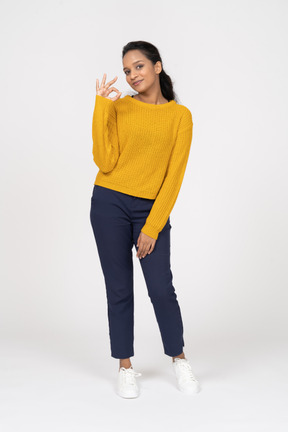 Front view of a happy girl in casual clothes showing ok sign and looking at camera