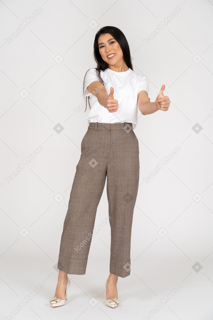 Vista frontal de uma jovem sorridente de calça e camiseta mostrando o polegar
