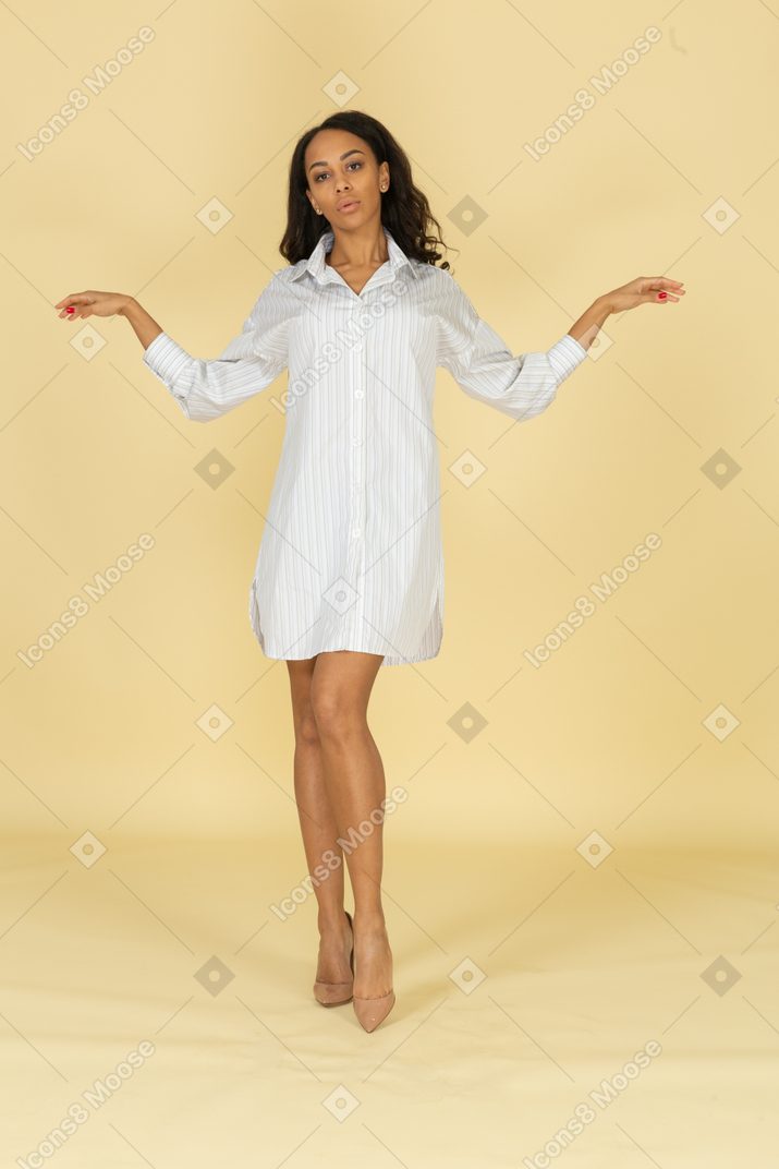 Vista frontal de una mujer joven de piel oscura con vestido blanco extendiendo sus manos