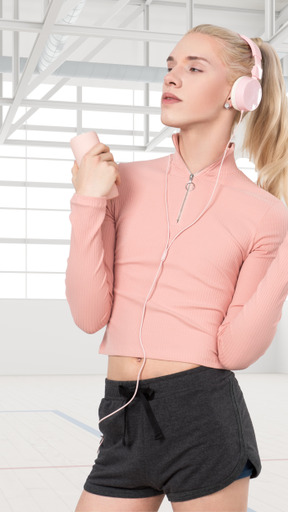 A young woman wearing a pink sweatshirt and headphones in a gym