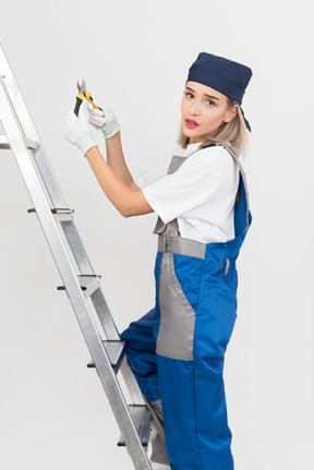 Female worker standing on stepladder and holding pliers