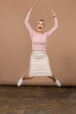 Вид спереди эмоциональной женщины в повседневной одежде, прыгающей с поднятыми руками