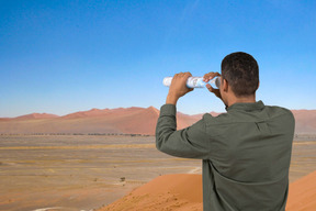 A man looking through rolled up map in the desert