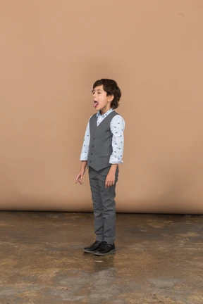 Cute boy in grey suit making faces and showing tongue