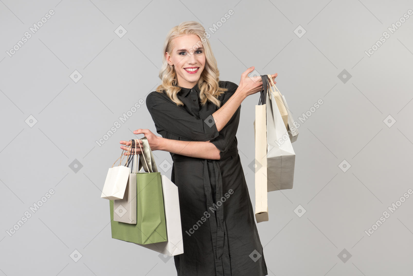 Молодой красивый белокурый человек в черном платье держит в руках кучу сумок