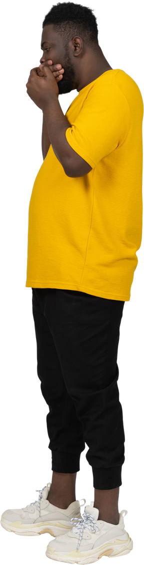 Vista lateral de um jovem chocado de pele escura em uma camiseta amarela escondendo a boca