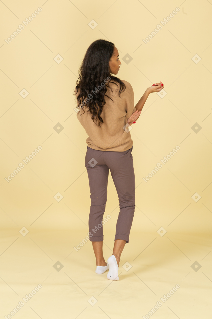Back view of a dark-skinned questioning young female raising hand