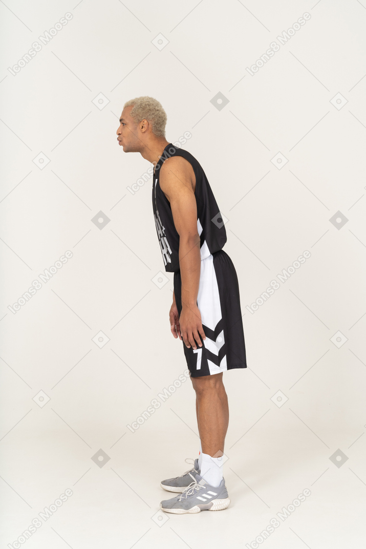 Vista lateral de um jovem jogador de basquete masculino assobiando, inclinando-se para a frente