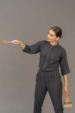 Woman in gray coveralls posing with paint brushes