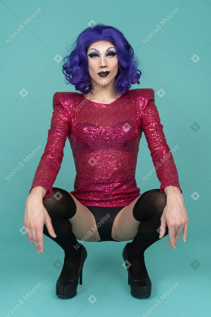 Portrait of a drag queen in pink sequin dress squatting with hands resting on knees