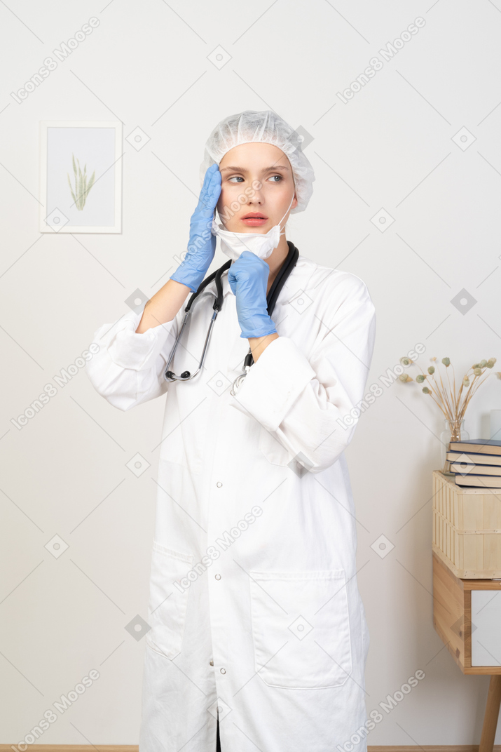 Vue de trois quarts d'une jeune femme médecin mettant un masque et regardant de côté