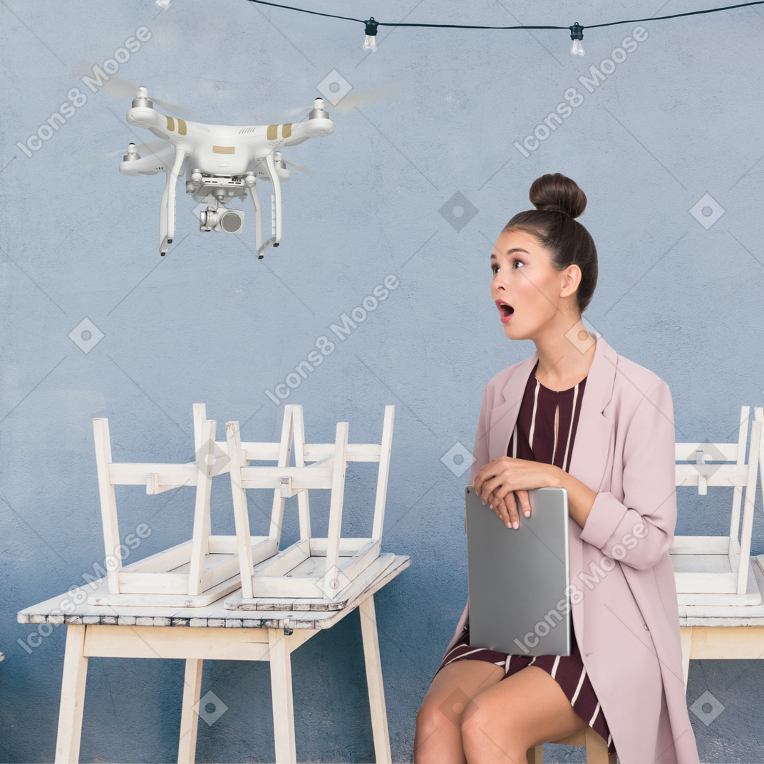 Surprised woman with laptop sitting on chair and looking at drone
