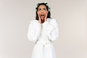 Young afrowoman in bathrobe and with hair curlers gasping