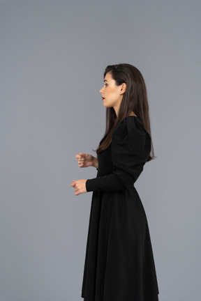 Vista lateral de uma jovem em um vestido preto levantando as mãos