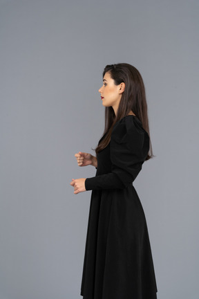 Side view of a young lady in a black dress raising her hands