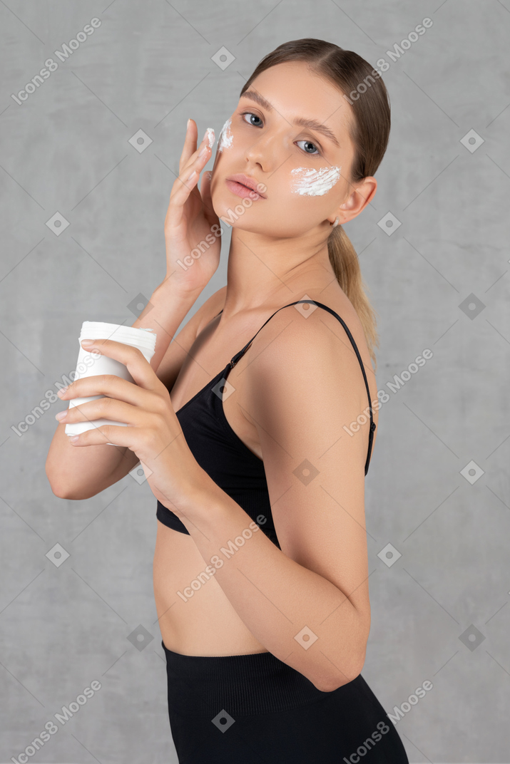 Giovane donna attraente che mette crema idratante sul viso