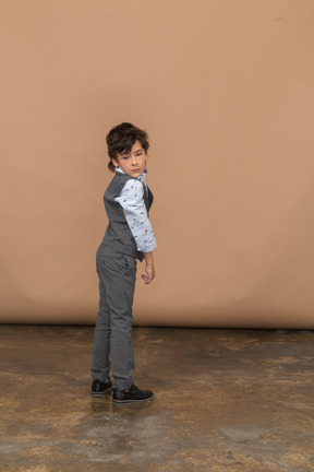 Vista lateral de um menino de terno cinza, olhando para a câmera