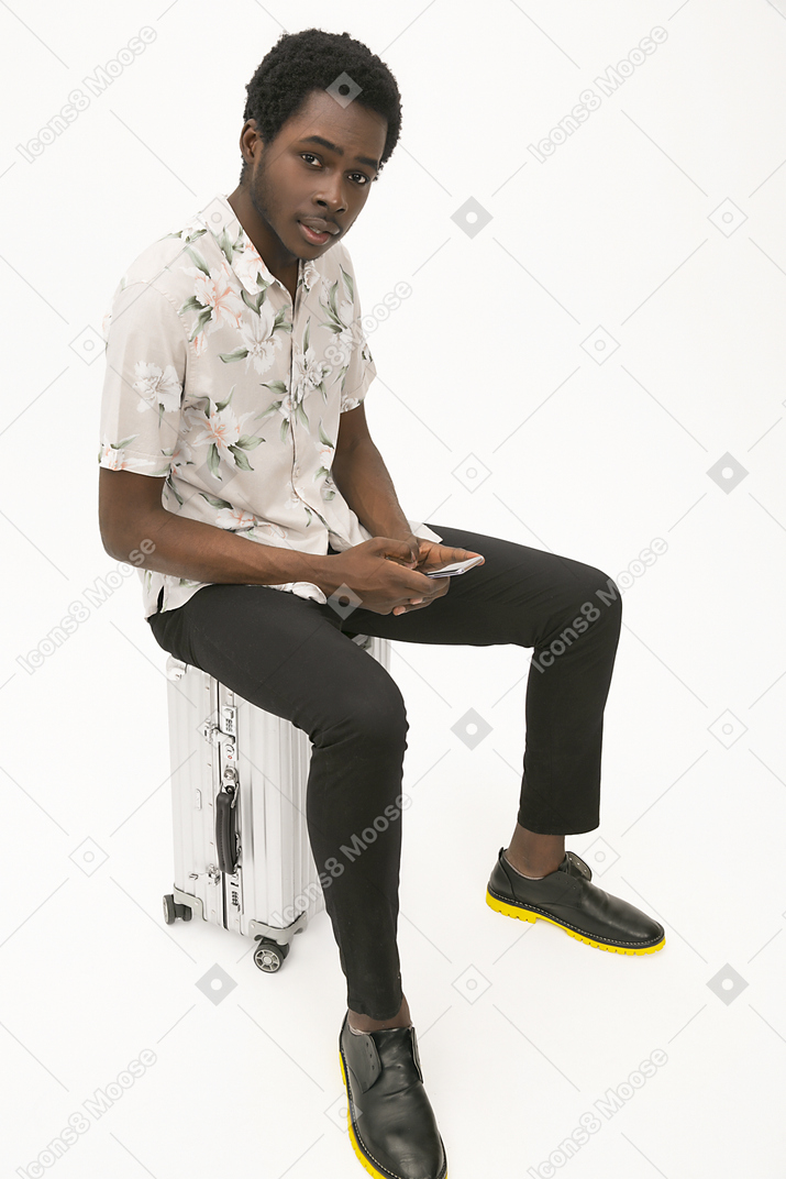 Afroman sitting on the baggage and using his smartphone