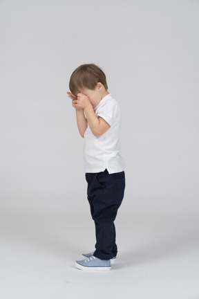 Side view of little boy covering his face with his hands