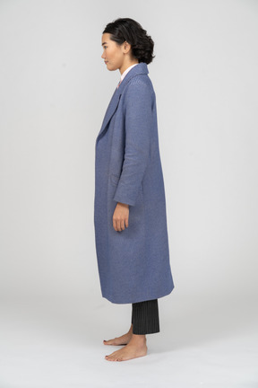 Side view of a woman in blue coat standing with arms at sides