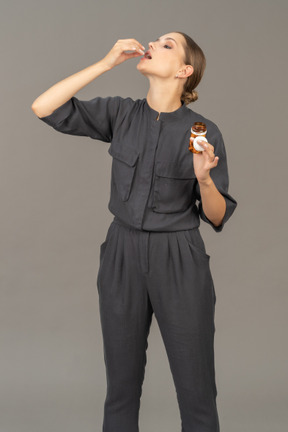 Vista frontal de uma jovem com um macacão tirando comprimidos de um frasco
