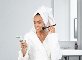 A woman in a bathrobe applying a face mask