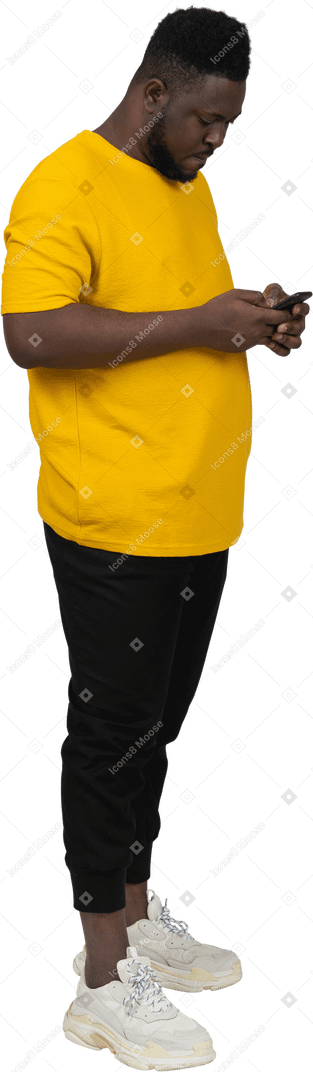 전화로 채팅하는 노란색 티셔츠를 입은 검은 피부의 젊은 남자의 3/4 보기