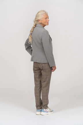 Rear view of an old woman in suit posing with hand on hip