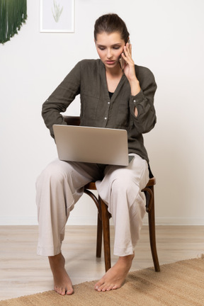 一位忙碌的年轻女子坐在椅子上，拿着笔记本电脑和手机的前视图