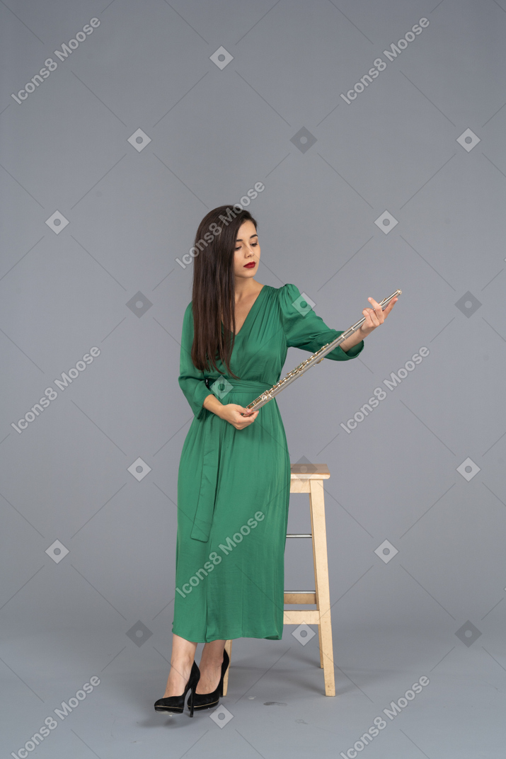 Vista frontale di una giovane donna in abito verde, seduta su una sedia e tenendo il clarinetto