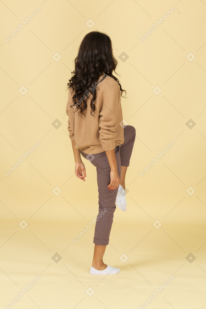 Three-quarter back view of a dark-skinned young female raising leg