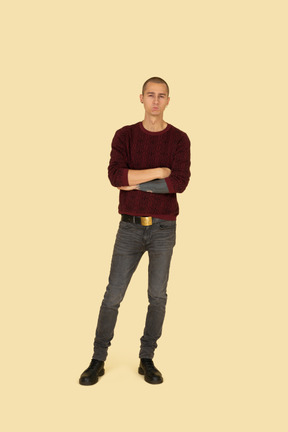 Front view of an offended young man dressed in casual clothes crossing his hands