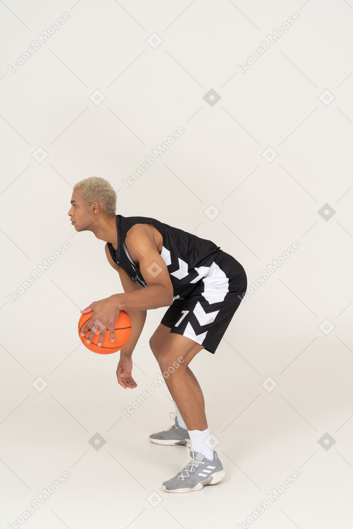 Vista laterale di un giovane giocatore di basket maschile che fa dribbling