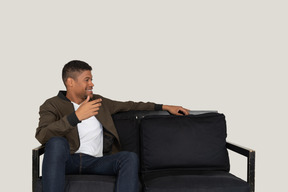 Smiling young man sitting on the sofa and telling something