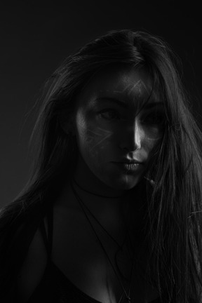 Close-up da silhueta escura de uma jovem com arte no rosto olhando de lado