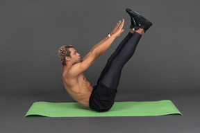 Vista laterale di un uomo afro senza camicia in equilibrio che alza le braccia e le gambe