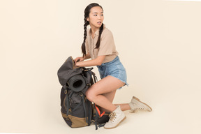 Young asian female traveller sitting near huge tourist backpack