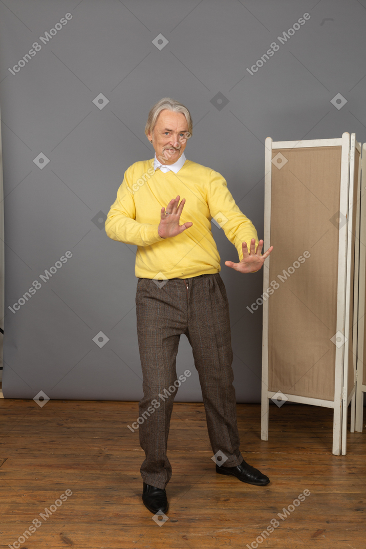 Front view of a shy smiling old man outstretching his hands