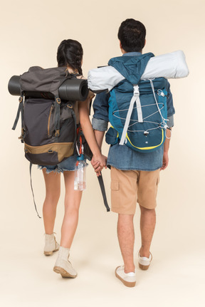 Young woman and man with backpacks holding hands