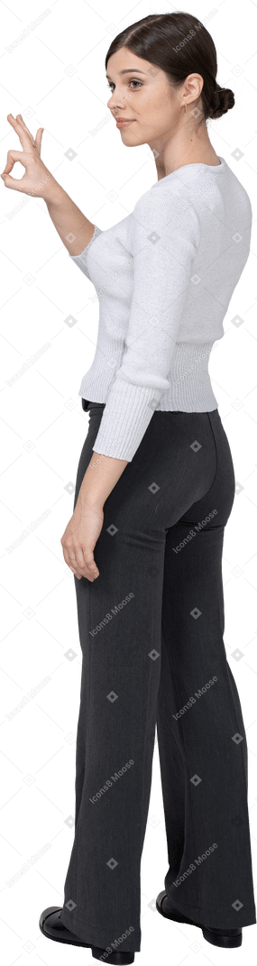 Three-quarter back view of a young woman in office clothing showing ok sign