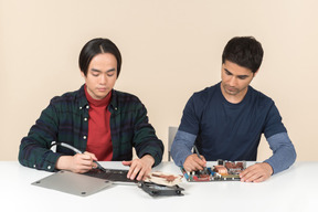 Two young geeks sitting at the table and fixing details on it