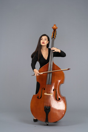 Vista frontal de una mujer joven vestida de negro tocando el contrabajo con un arco