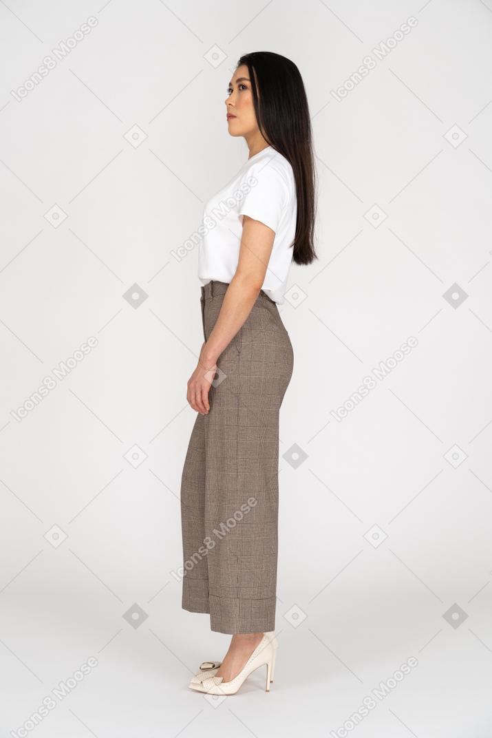 Vista lateral de una mujer joven en pantalones de pie quieto mientras mira a un lado